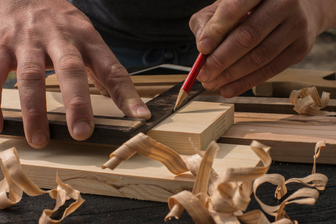 A picture of a man carving and measuring a piece of wood.